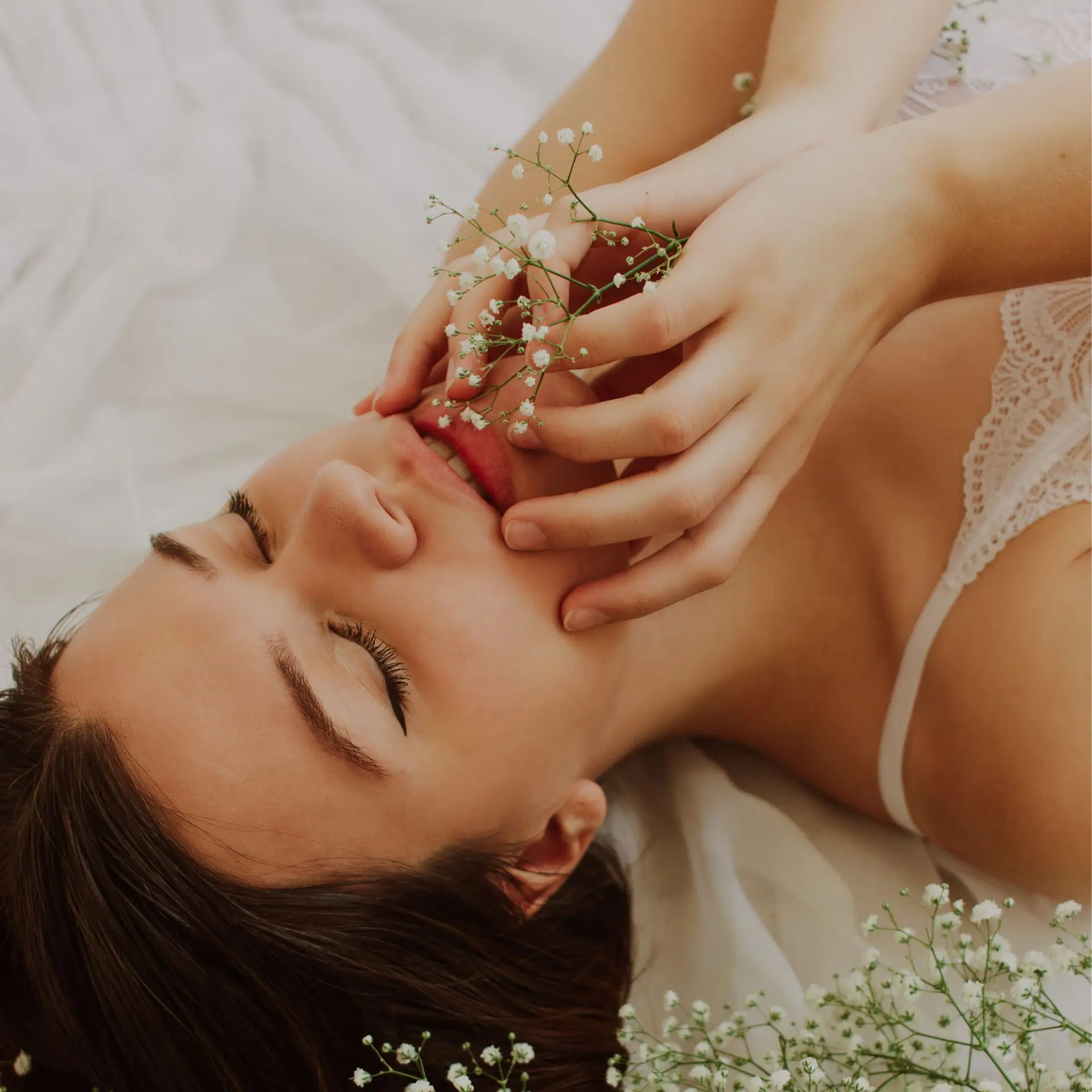 A woman lying on the back with hands in her face and flowers around her